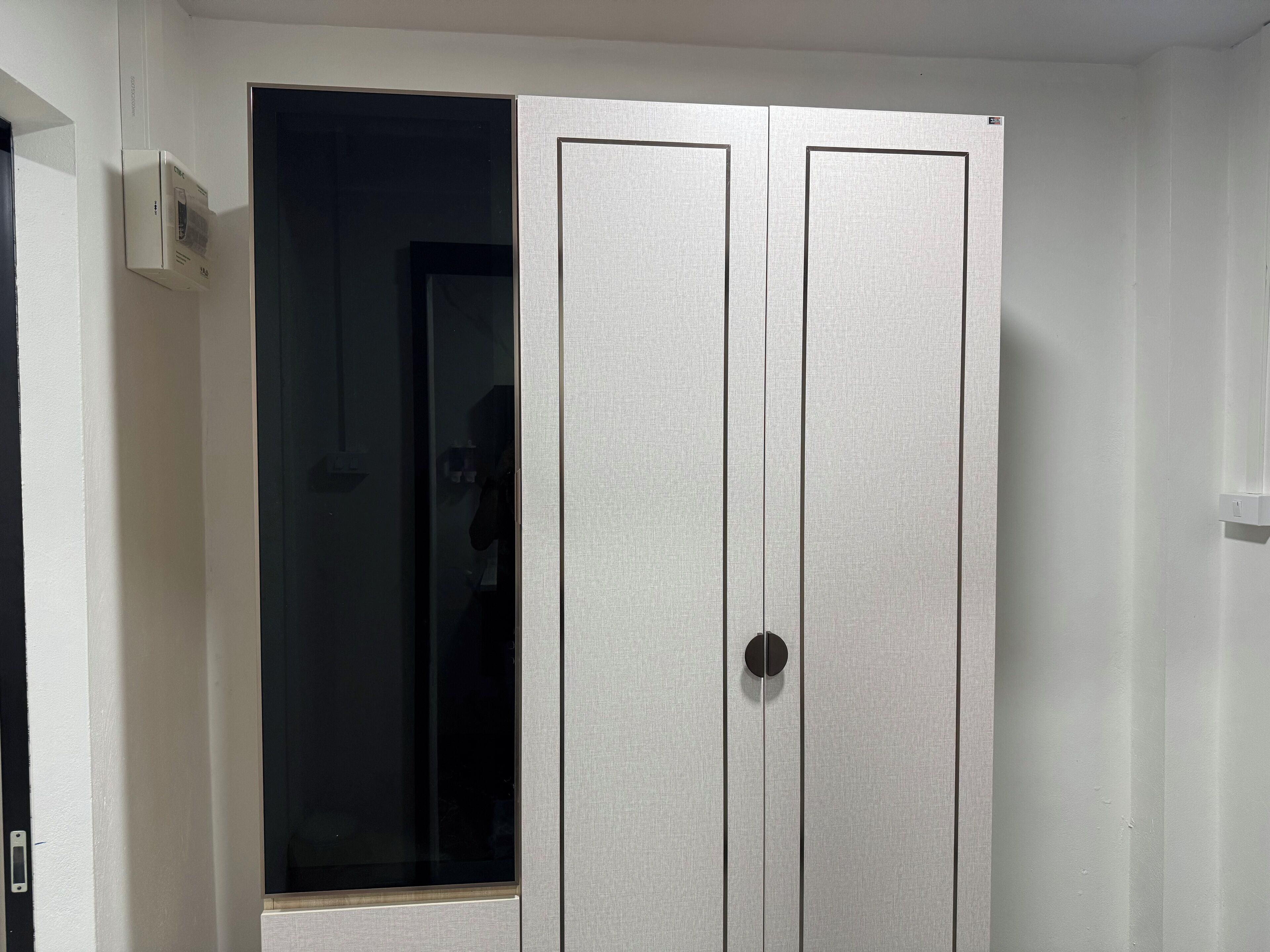 A white wardrobe with a mirror and a black circular handle.