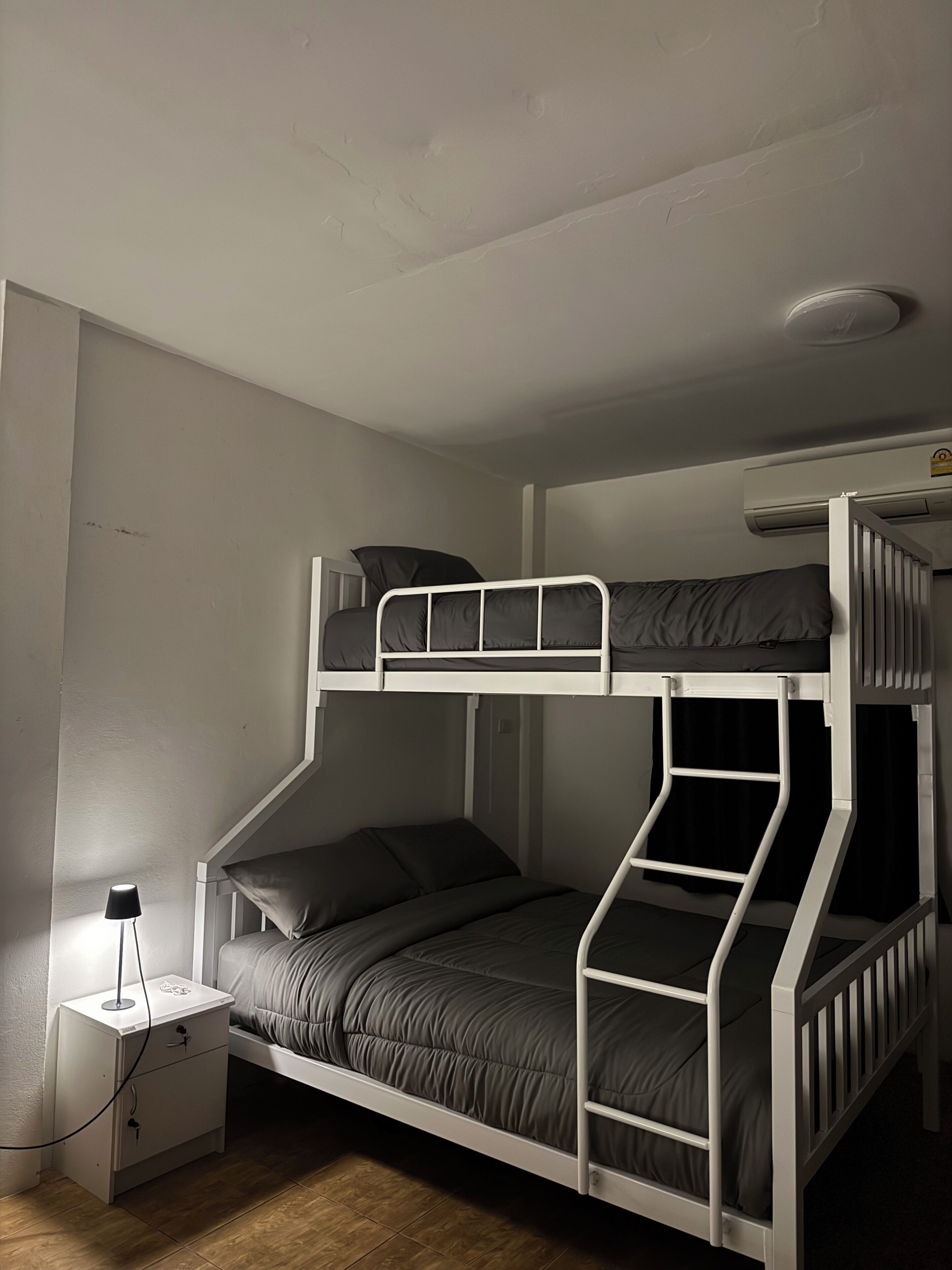 A bunk bed with a desk and lamp, white walls, and a ceiling vent.