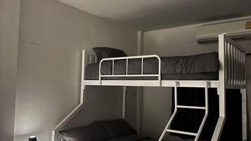 A bunk bed with a desk and lamp, white walls, and a ceiling vent.