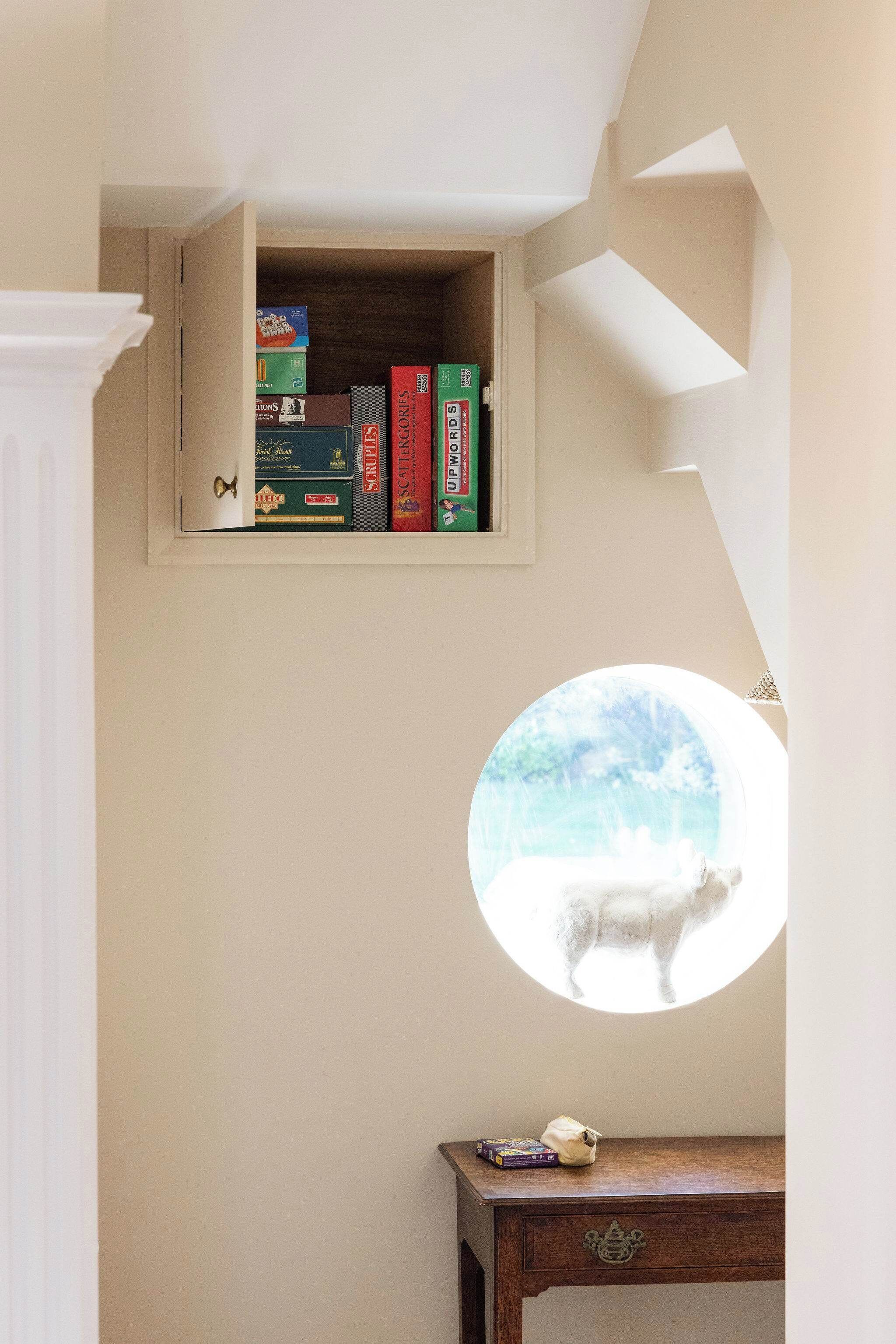 A room with a bookshelf containing books and a circular window with a view of a white animal.