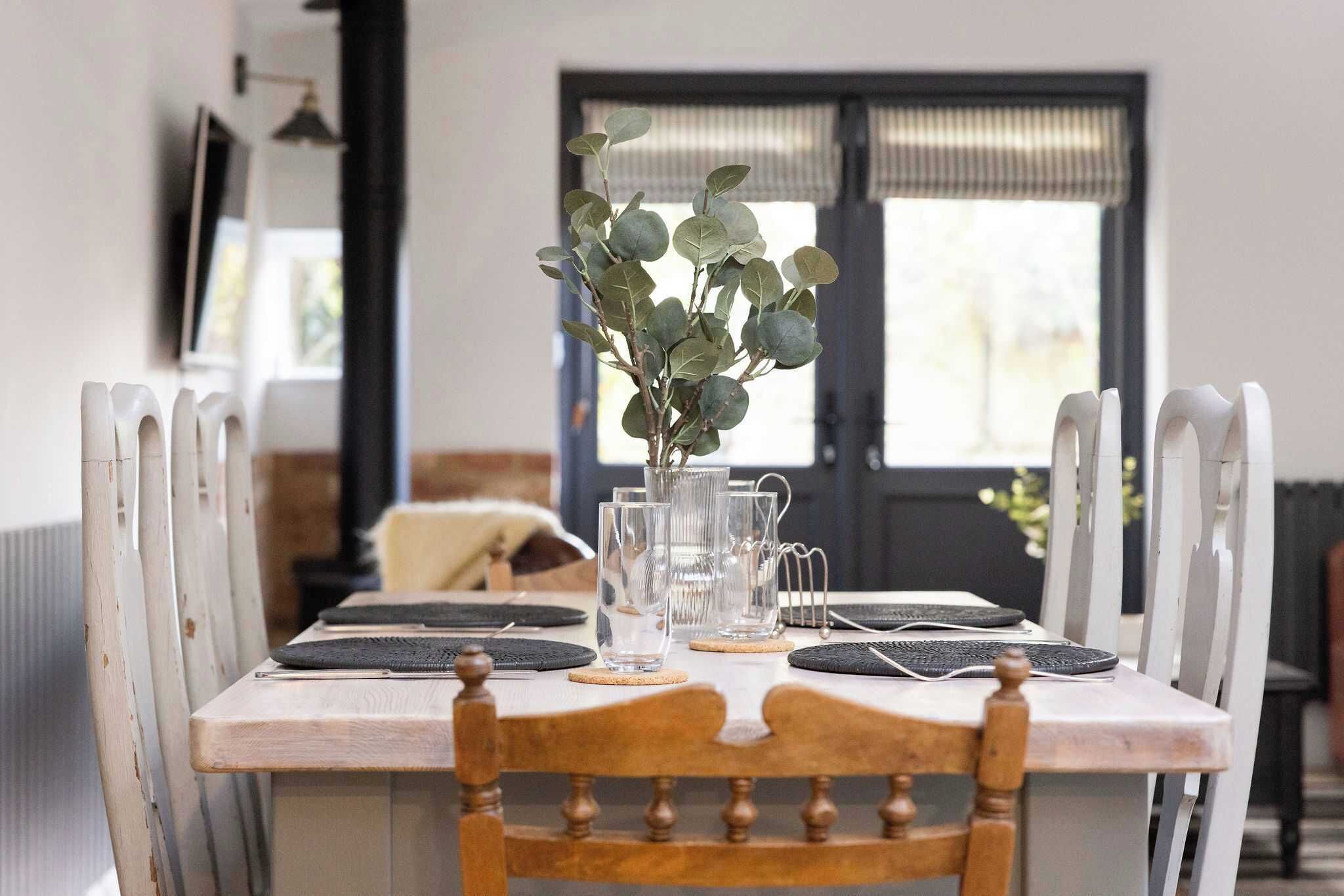 A dining table set with clear glassware, a vase with green foliage, and a black placemat.