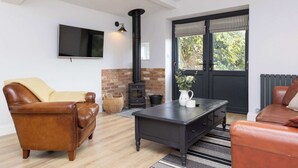 Ein gemütliches Wohnzimmer mit Ledersofas, einem schwarzen Tisch, einem an der Wand befestigten Fernseher, einem schwarzen Kaminofen und einer schwarzen Tür mit Fenster.