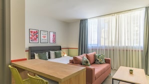 Habitación de hotel con cama, sofá, una mesita y un escritorio. Se observan tres cuadros en la pared.