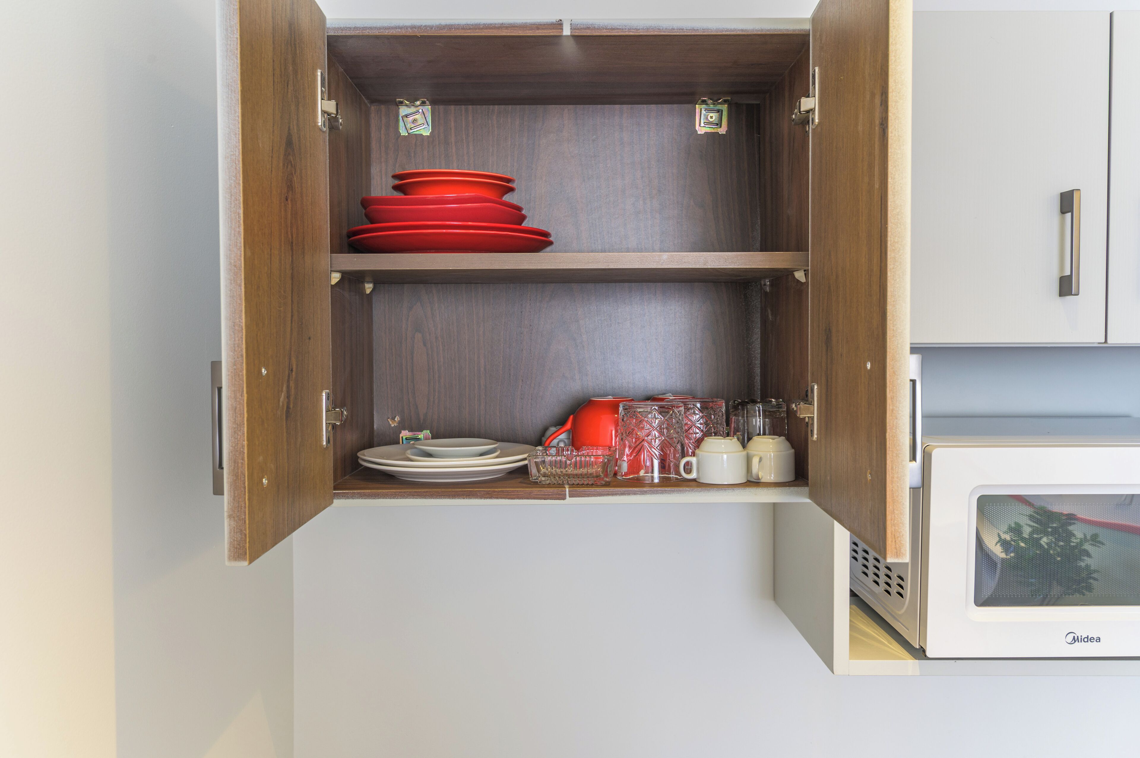 Una cocina con armarios de madera, un microondas y diferentes platos y utensilios.