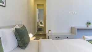 Una habitación de hotel moderna con una cama bien tendida, una mesita de noche con lámpara, una planta pequeña y un escritorio integrado con una silla.