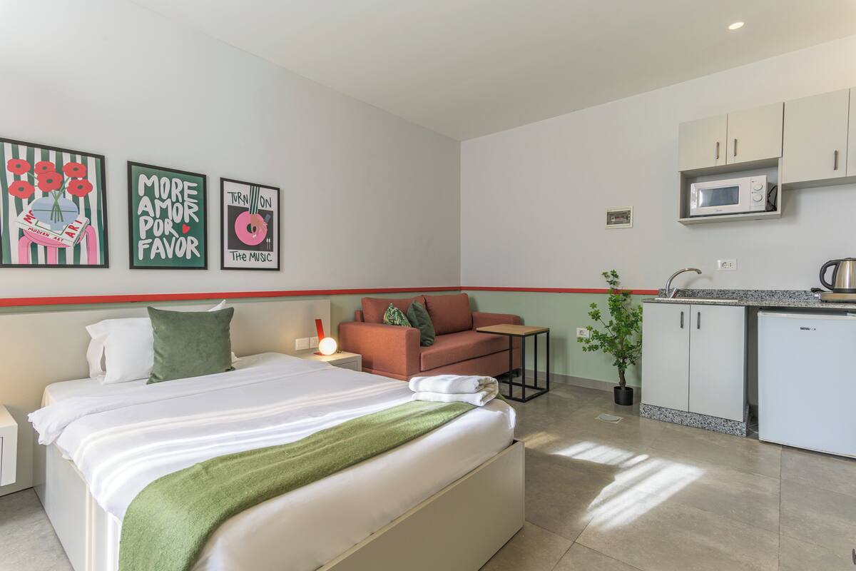 A hotel room with a bed, a sofa, a small table, a microwave, and a refrigerator.
