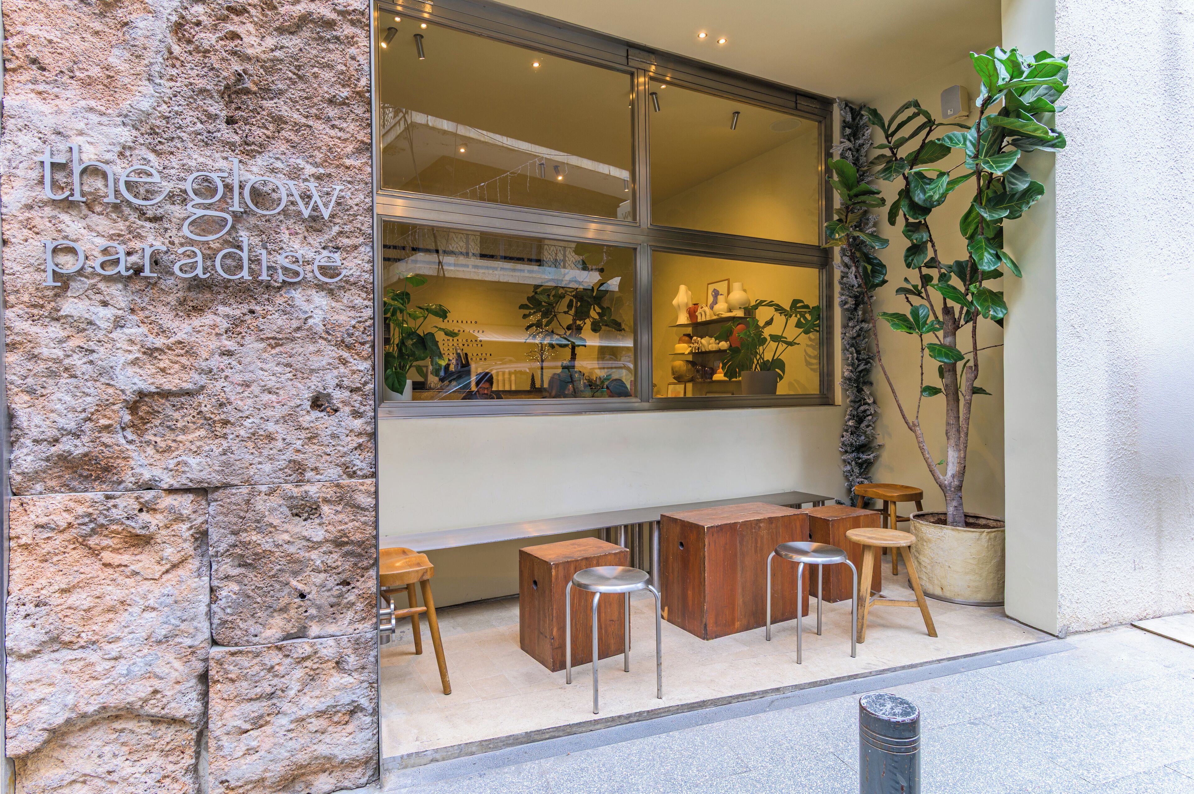 A storefront with a stone facade, a large window, and outdoor seating with stools and tables.