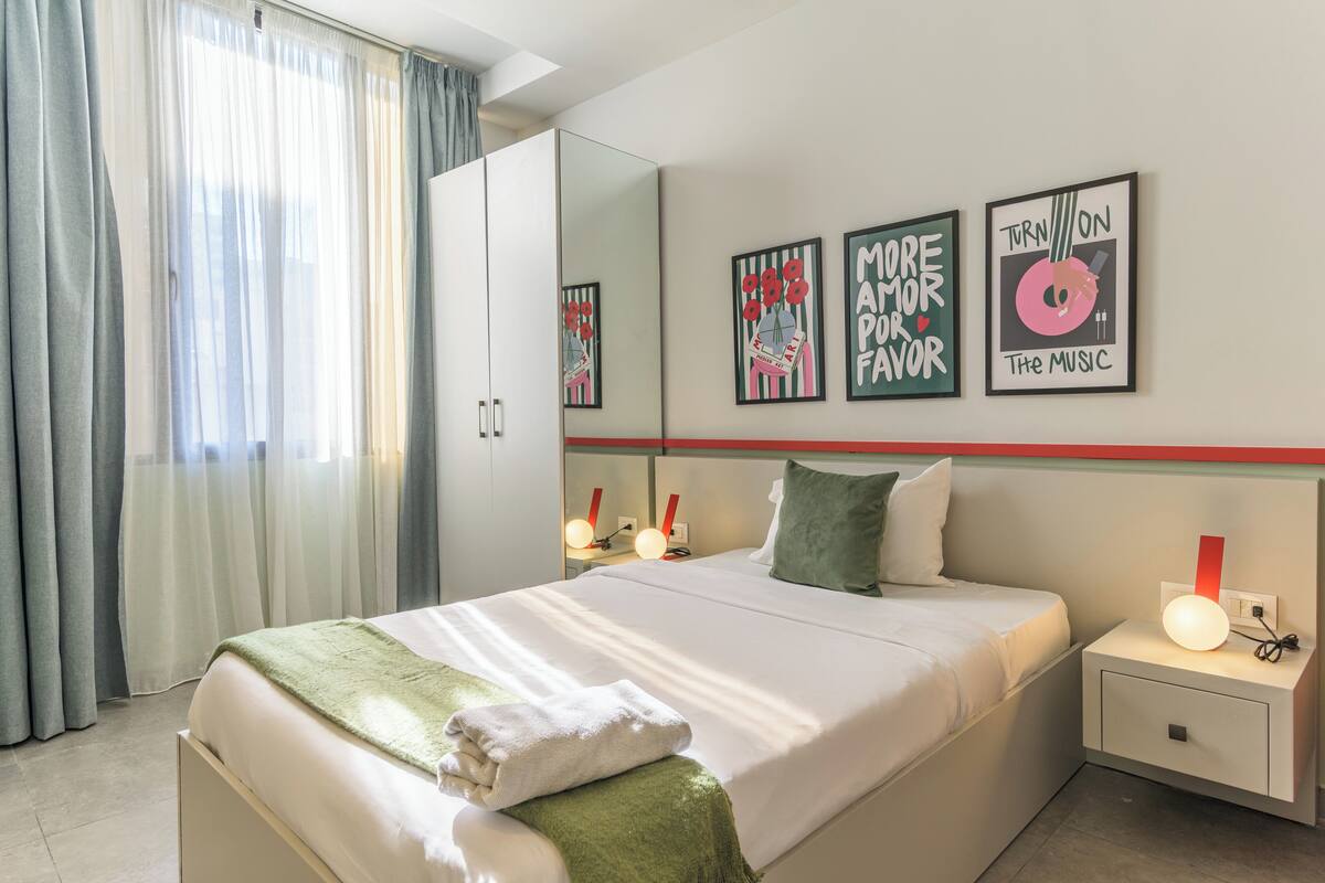 A hotel room with a bed, a nightstand, a mirror, and artwork on the wall.