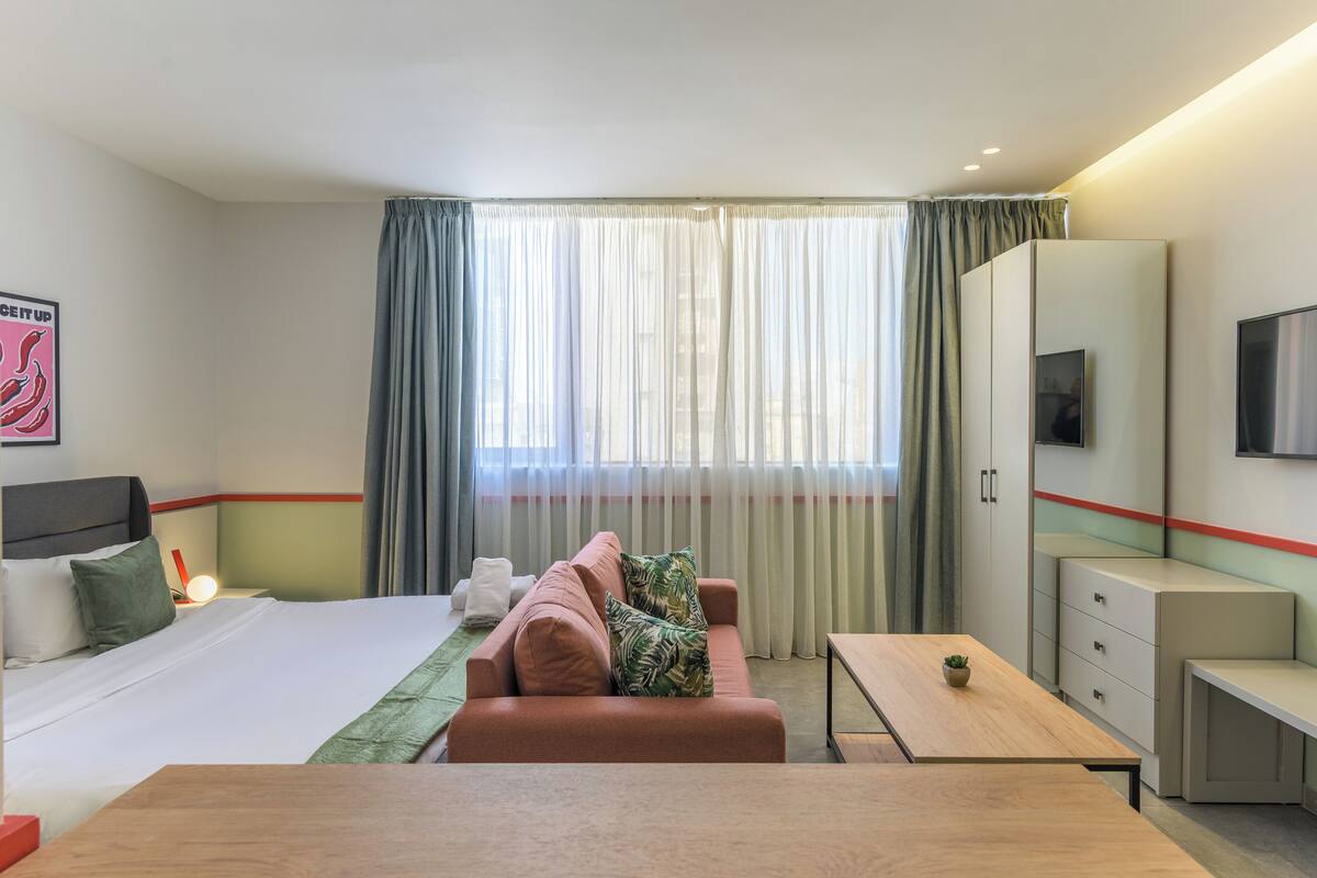A hotel room with a bed, a sofa, a desk, a TV, and a wardrobe.