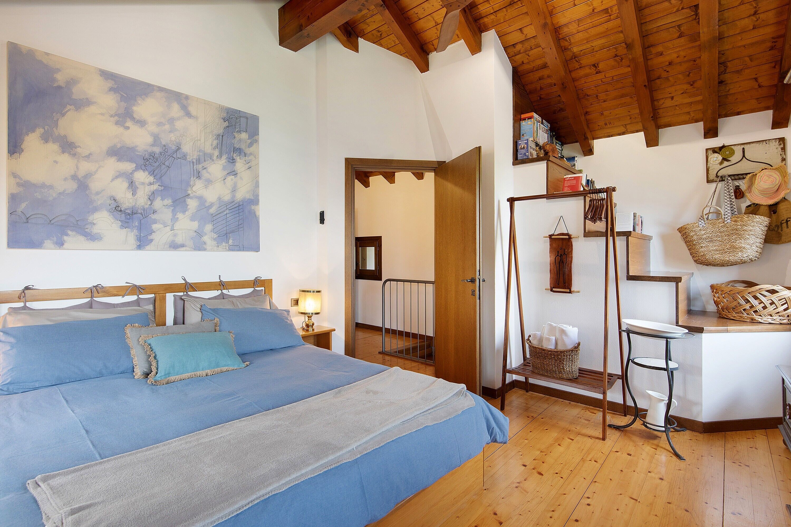 Una camera da letto con un letto, un comodino, una lampada a parete, un soffitto in legno e un quadro di grandi dimensioni.