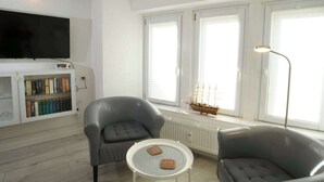 Een moderne woonkamer met een flatscreen televisie, leren fauteuils, een klein rond tafeltje en een boekenplank.