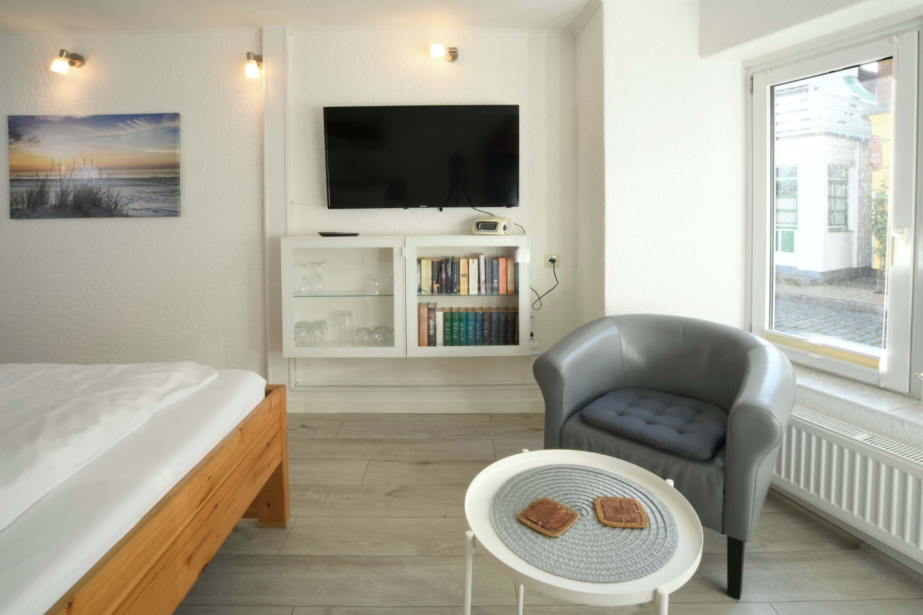 A bedroom with a bed, a TV, a bookshelf, a chair, and a small table.