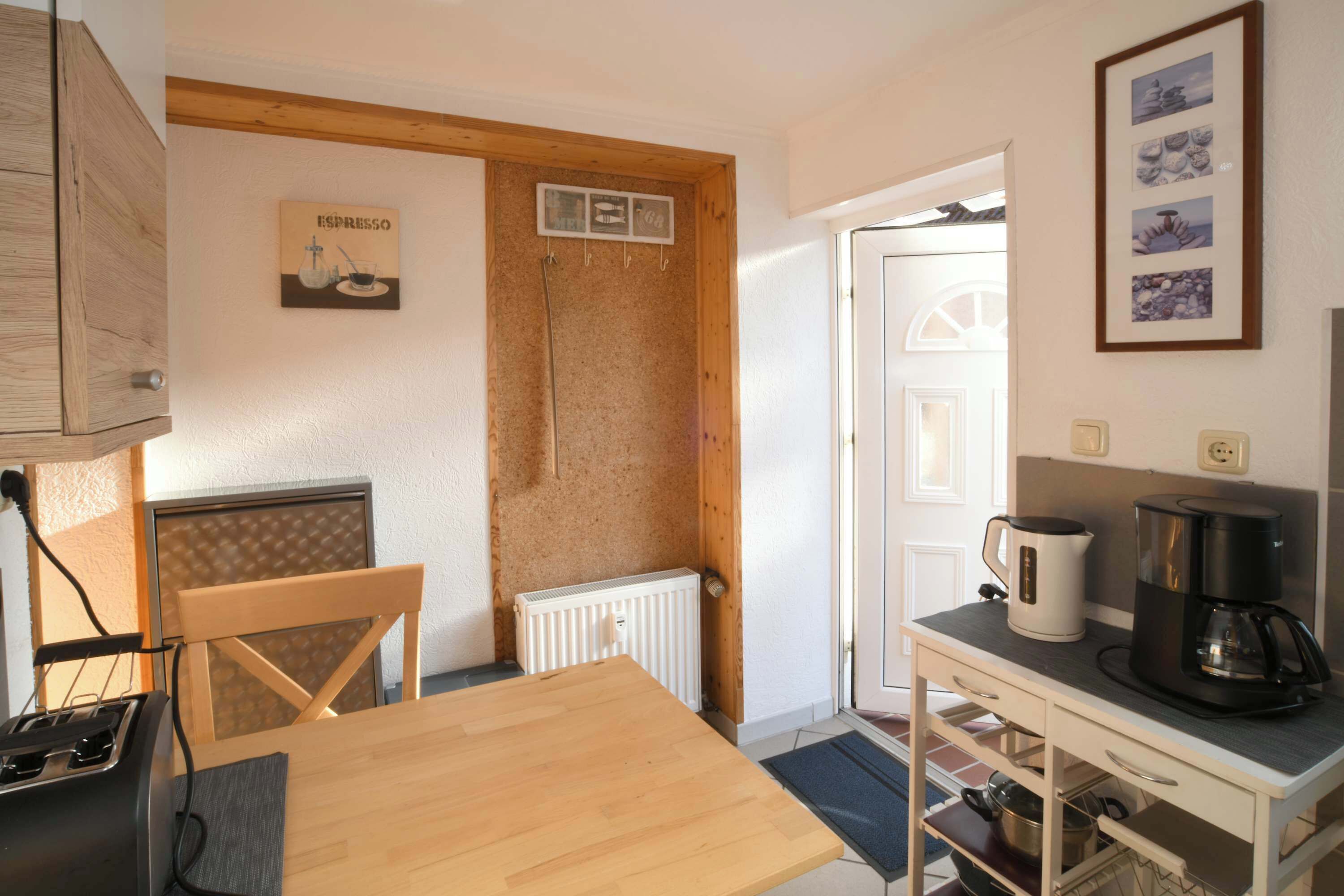 Une petite cuisine avec une table en bois, une machine à café et une bouilloire posées sur un plan de travail blanc.