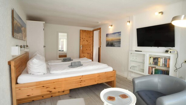 Een slaapkamer met een houten bed, een televisie, een boekenkast en een klein tafeltje.