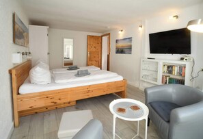A bedroom with a wooden bed, a television, a bookshelf, and a small table. - Apartment Muschelbude (Rostock)