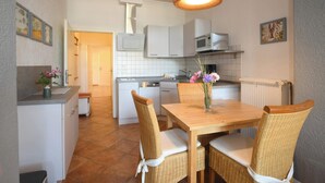 Een keuken met witte kastjes, een houten eettafel, rieten stoelen en een hanglamp.