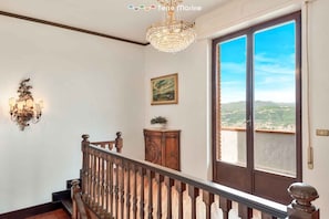 Ein geräumiges Zimmer mit einer Holztreppe, einem Chandelier, einem großen Fenster mit Aussicht und einem Gemälde an der Wand.