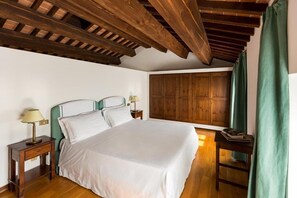 A bedroom with a large bed, wooden headboard, two bedside tables with lamps, a wooden wardrobe, and a green curtain. - Serego Alighieri (Sant'Ambrogio di Valpolicella)
