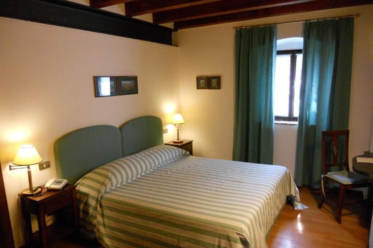A hotel room with a large bed, two bedside lamps, a wooden chair, and a window with curtains.