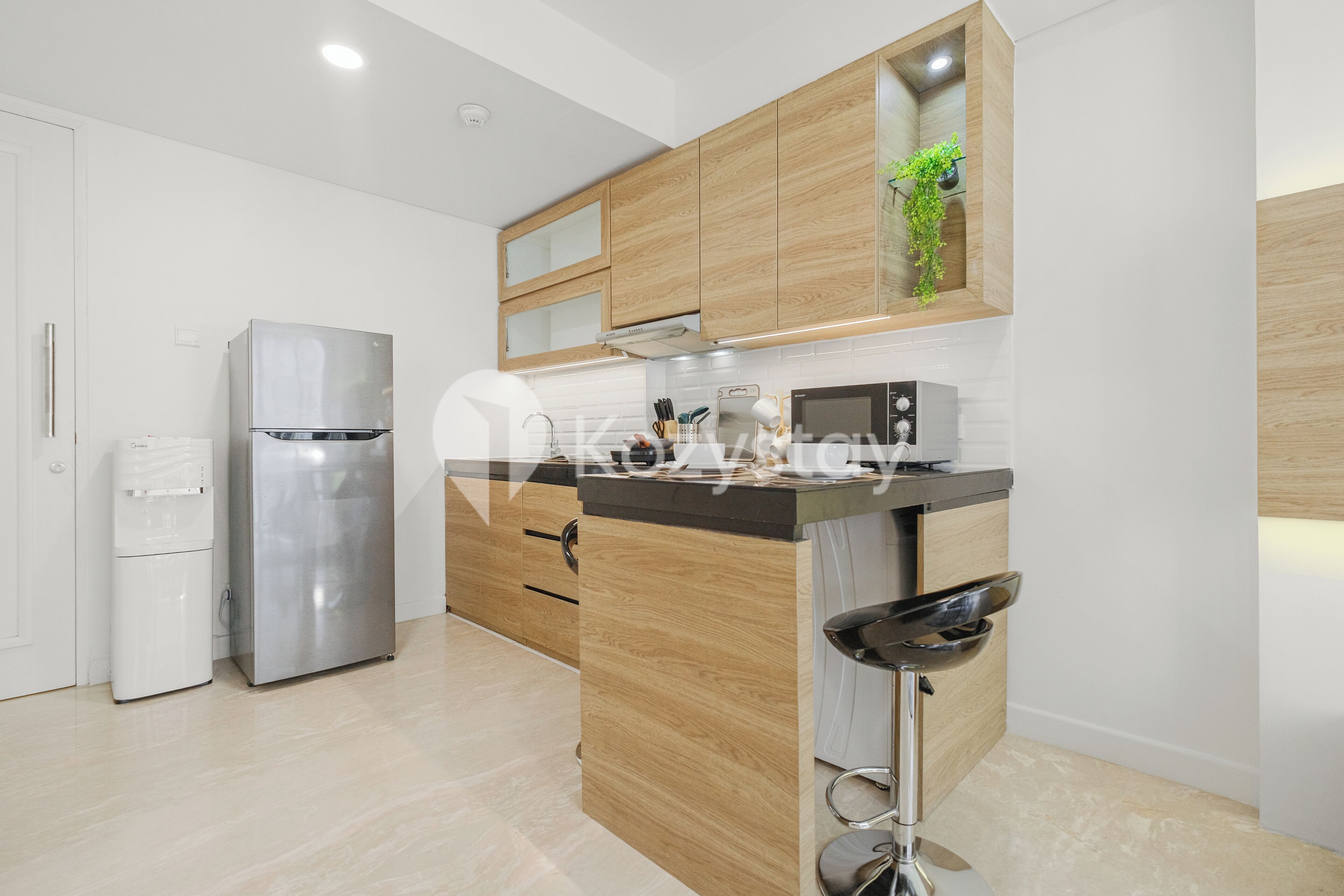 A modern kitchen with wooden cabinets, a stainless steel refrigerator, a microwave, and a bar stool.