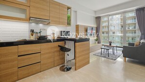 Una cocina moderna con armarios de madera, encimera negra y un taburete de bar. Hay una zona de comedor con una mesa y sillas, y un ventanal con cortinas.