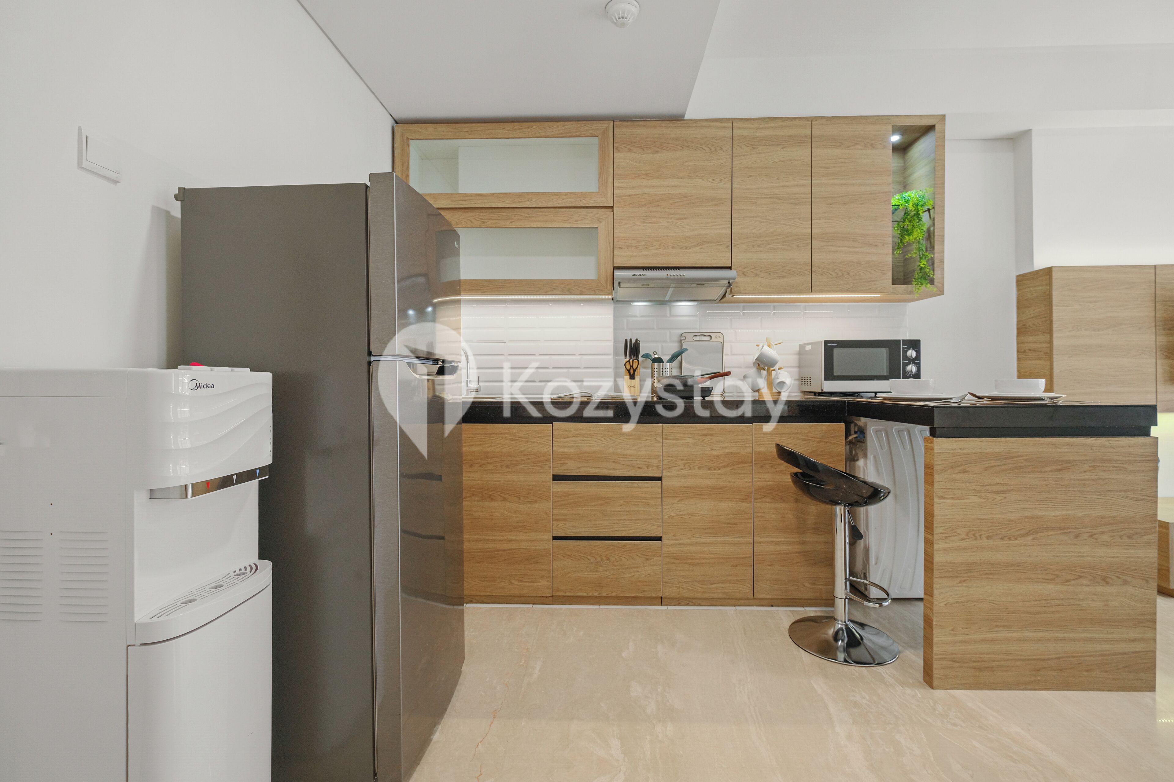 A modern kitchen with wooden cabinets, a stainless steel refrigerator, a microwave, and a bar stool.