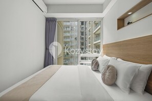 Une chambre d’hôtel moderne avec un grand lit, une tête de lit en bois et une vue sur les gratte-ciel, visible à travers une grande fenêtre.