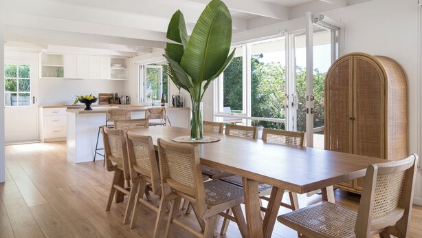 Una cocina amplia con una gran mesa de comedor, sillas de mimbre y una planta en el centro.