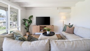 Una sala de estar moderna con un ventanal grande, un televisor de pantalla plana, un mueble de madera y un sofá cómodo.
