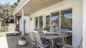 Un patio al aire libre con una mesa y sillas de madera, rodeado de amplias ventanas.