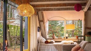 Una habitación acogedora con una mesa de vidrio, velas, un sofá y una ventana con vistas a árboles.