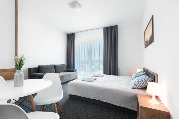 A bright bedroom with two neatly made beds, soft gray accents, and large windows letting in natural light.