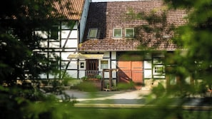 Ein traditionelles Fachwerkhäuschen mit auffälligem Eingangsbereich, einer kleinen Veranda mit Blumentöpfen und einem Ziegelweg, der zur Tür führt.
