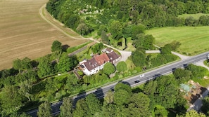 Vue aérienne d’une propriété rurale comprenant une grande maison, une route et des champs environnants.