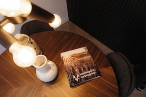 Ein runder Holztisch mit einer weißen Vase, einem Buch mit dem Titel 'Veluwepark de Bosgraat' und einer Lampe mit mehreren Glühbirnen.