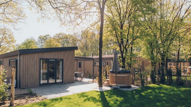 Una casa moderna con un patio, un jacuzzi de madera y un césped cuidado.