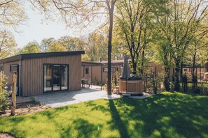 Una casa moderna con un patio, un jacuzzi de madera y un césped cuidado.