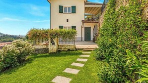 Ein zweistöckiges Haus mit einer Stein-Fassade, einem Balkon und einem gepflegten Garten mit einem Kiesweg zum Eingang.