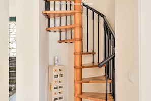 A wooden spiral staircase with black railings and a white wall.