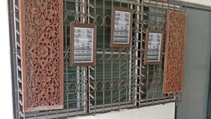 A small outdoor seating area with a round table and two chairs, a decorative metal fence, and framed pictures on the fence. - OhoWowGood Home Stay Chiangmai room 101 (Tambon Fa Ham)