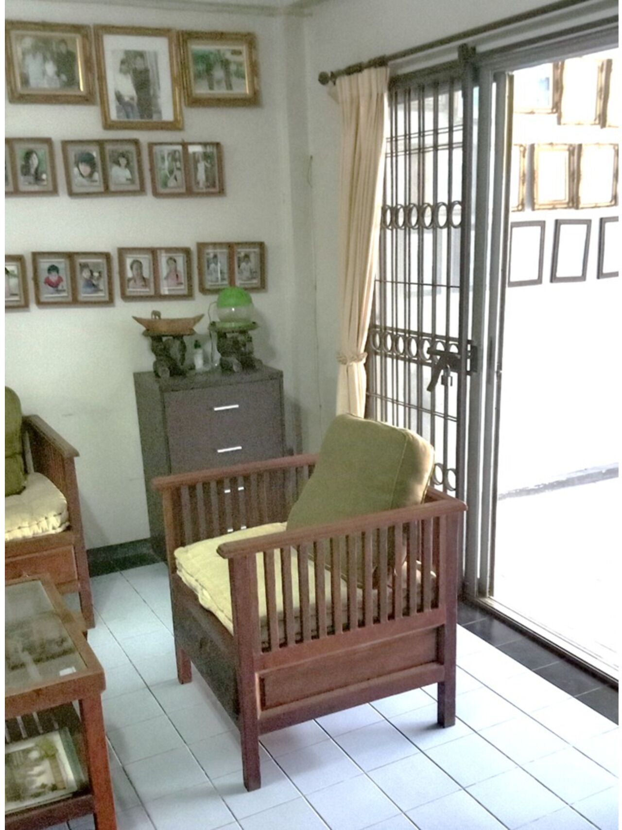 A room with a wooden chair, a small cabinet, and a window with a metal gate.