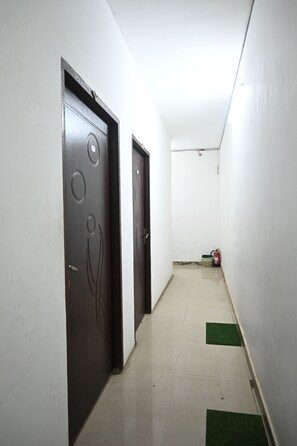 A narrow hallway with white walls and a tiled floor, featuring two doors with circular designs and a fire extinguisher near the end. - The Kashi Palace (Varanasi)
