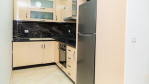Eine kleine Küche mit beigen Schränken, einer schwarzen Arbeitsplatte, einem Einbauofen und einem Kühlschrank.