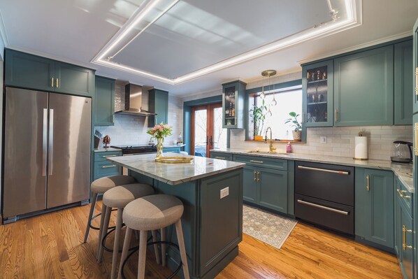 A modern kitchen with teal cabinets, a stainless steel refrigerator, and a central island with bar stools. - The Craftsman - Handcrafted escape on Pond 2BR 2BA (Norfolk)
