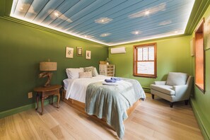 A bedroom with a bed, a chair, a lamp, and a window. - The Craftsman - Handcrafted escape on Pond 2BR 2BA (Norfolk)