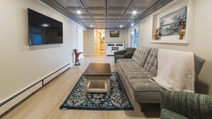 A living room with a flat-screen TV, a sofa, a coffee table, and a patterned rug. - The Craftsman - Handcrafted escape on Pond 2BR 2BA (Norfolk)