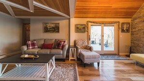 A cozy living room with a wooden ceiling, a sofa with patterned cushions, a small table, and a chair. - The Craftsman - Handcrafted escape on Pond 2BR 2BA (Norfolk)