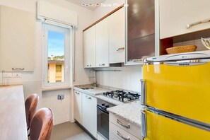 A kitchen with white cabinets, a yellow refrigerator, a gas stove, and a window with a view of buildings. - Welcome to Bellini13 in La Spezia, our new holiday home recently renovated and ready to welcome you for an unforgettable stay! The interiors have been renovated with pastel colors that create a relaxing and serene atmosphere and with wallpaper that adds  (La Spezia)