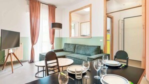 A dining area with a table set for four, a sofa, a TV, and a mirror. - Welcome to Bellini13 in La Spezia, our new holiday home recently renovated and ready to welcome you for an unforgettable stay! The interiors have been renovated with pastel colors that create a relaxing and serene atmosphere and with wallpaper that adds  (La Spezia)