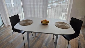 A dining table with two chairs, a bowl of fruit, and a window with curtains.